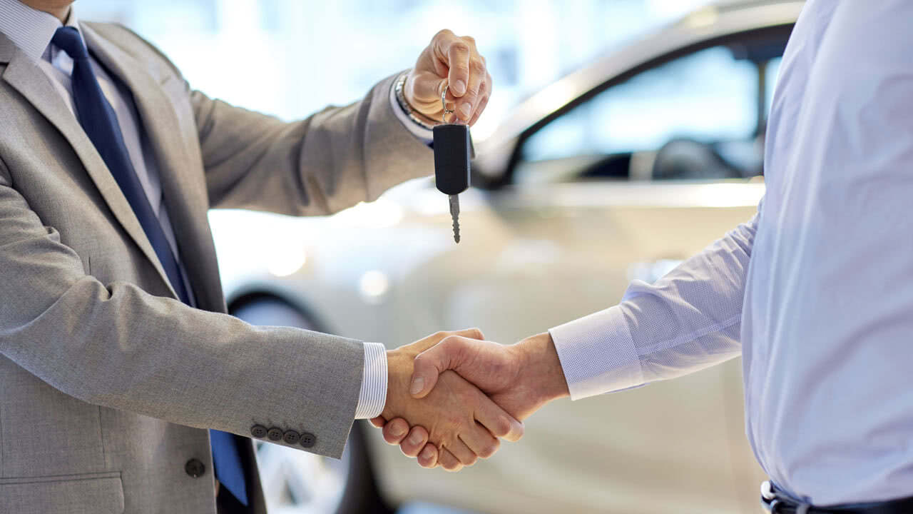 Mann erhält die Autoschlüssel von einem Neuwagen. Laut einer Studie, möchten weniger Menschen im Jahr 2023 ein auto kaufen.