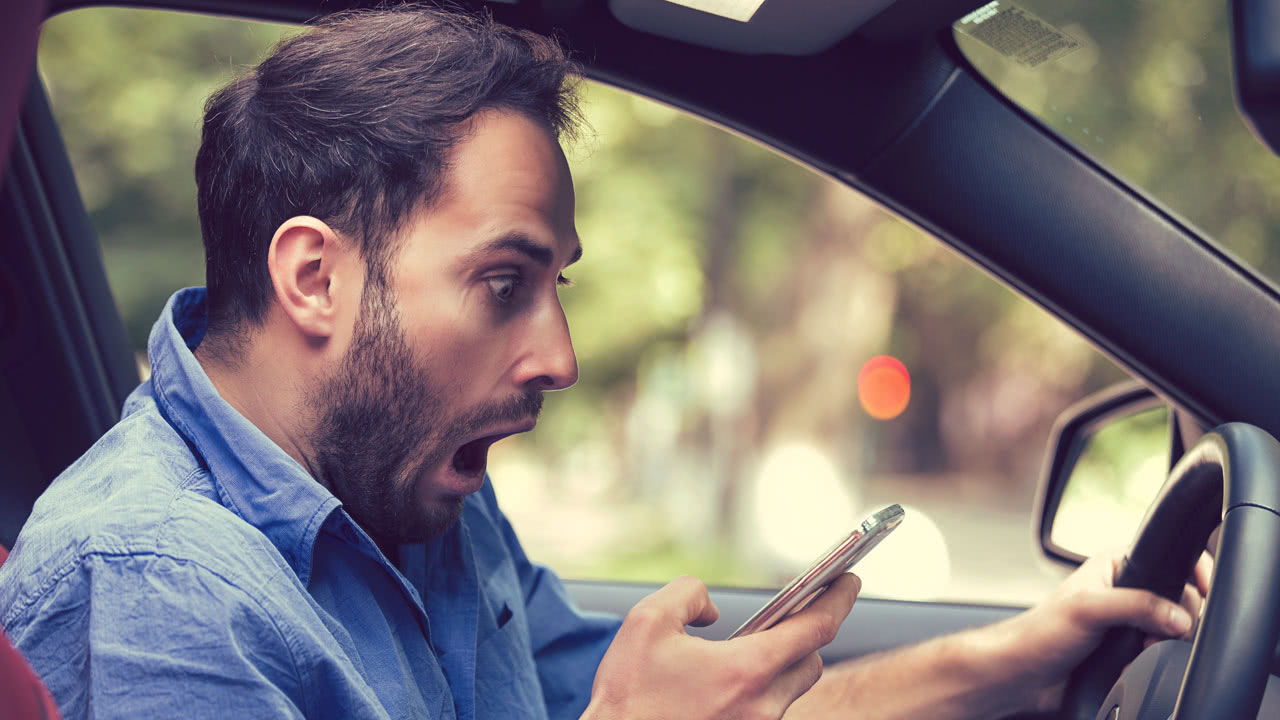 Mann ist überrascht als er die Irrtümer aus dem Straßenverkehr auf sein Handy im Auto entdeckt.