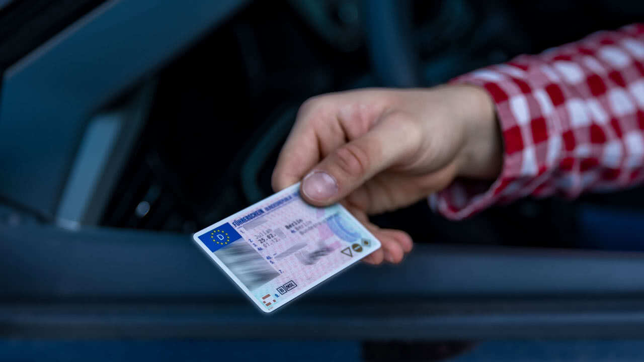 Fahrer zeigt seinen Führerschein aus dem Auto. Die EU plant neue Führerscheinrichtlinien, weshalb das bald auch per App möglich sein soll.