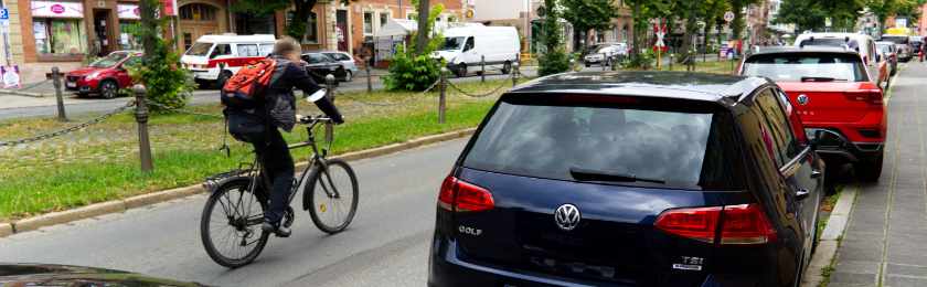 Ein Radfahrer fährt an parkenden Autos vorbei. In Berlin werden zukünftig weitere Parkplätze eingespart.