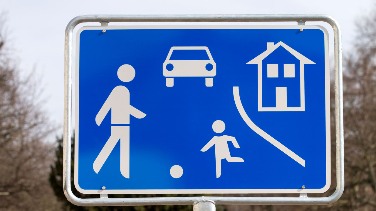 Verkehrsschild zeigt eine Spielstraße auf und informiert Autofahrer über eine Schrittgeschwindigkeit.