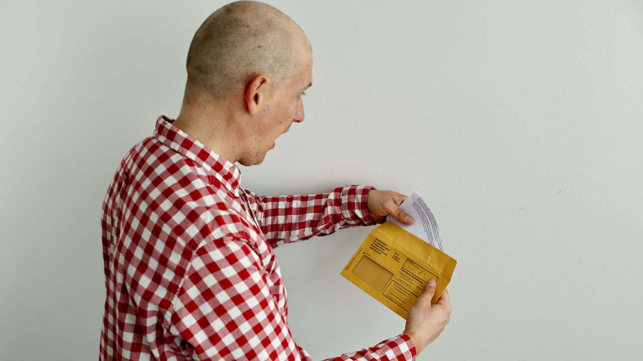 Mann öffnet einen gelben Briefumschlag mit einem Bußgeldbescheid. Er ist erschrocken, wie viele anderen Menschen in Deutschland wusste er nicht, dass er sich über Geblitzt.de helfen lassen kann.